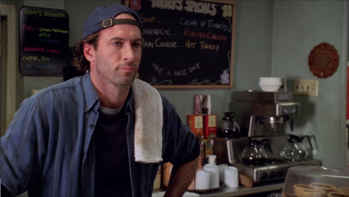 Luke Danes stoically standing behind the coffee bar. In the background is a Bunn RL35 filter coffee maker. It's stainless steel surface gleams in the diner light.