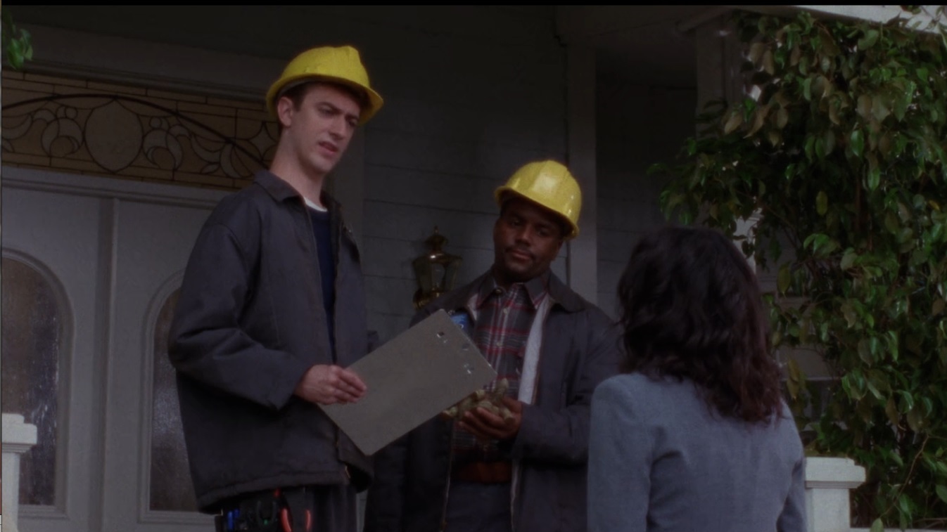 Kirk/Mick standing with another DSL installer on Loerlais's deck. They both wear yellow hard hats and navy overalls. Mick/Kirk is reacting incredulously to something Lorelai just said.